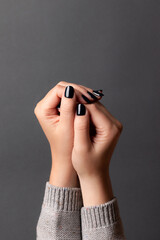 Female hands in gray knitted sweater with beautiful manicure - dark black nails on gray background. Nail care concept