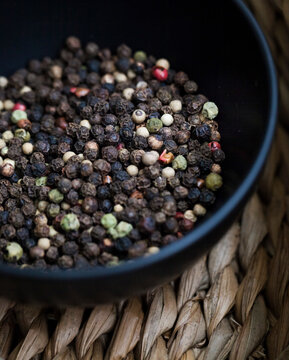 a bowl of peppercorns on wicker board