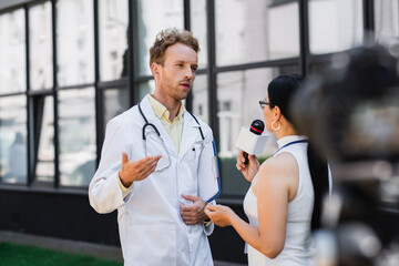 doctor in white coat gesturing while giving interview to asian journalist with microphone