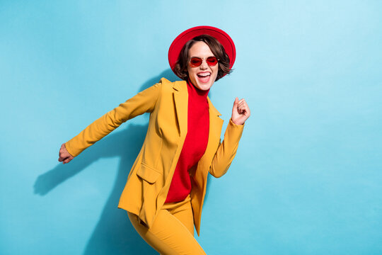 Photo of funny shiny young lady wear yellow blazer red cap eyewear smiling dancing isolated blue color background