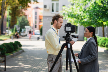 side view of newscaster holding microphone near asian businesswoman in glasses on street