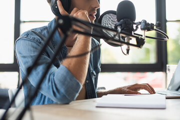 cropped view of radio host adjusting headphones and talking while making podcast
