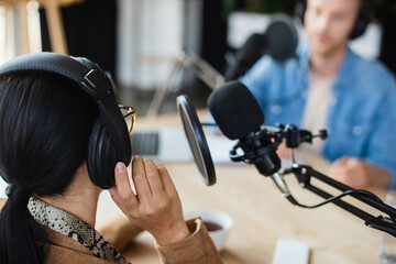 radio host in glasses adjusting headphones near blurred colleague