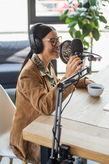 cheerful asian radio host in glasses and headphones talking during podcast