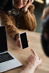 cropped view of blurred radio host pointing at smartphone near cheerful colleague