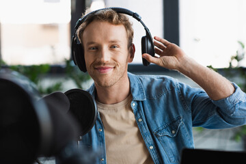 happy influencer adjusting headphones while making podcast in studio