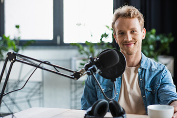 happy influencer looking at camera near microphone in studio