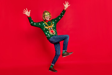 Photo of impressed funky young man wear green sweater spectacles smiling dancing walking isolated red color background
