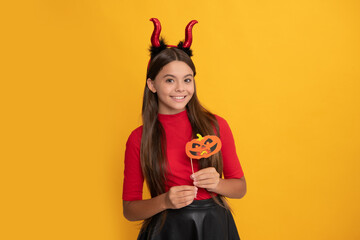happy kid with pumpkin party accessory wearing devil horns on yellow background, happiness