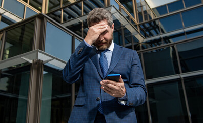 nervous entrepreneur in businesslike suit looking at phone outside the office, anxiety