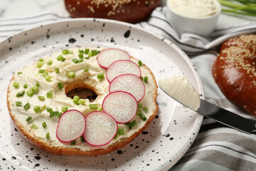 Delicious bagel with cream cheese, green onion and radish on plate, closeup