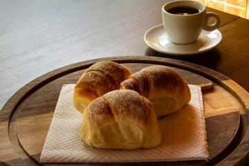 Três pães caseiros sobre uma tábua e uma xícara de café preto. Café da manhã.