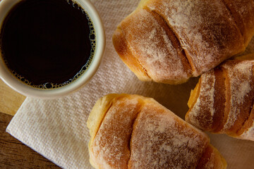Três pães caseiros sobre uma tábua e uma xícara de café preto. Café da manhã.