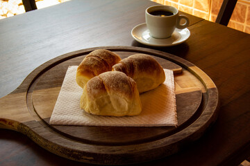 Três pães caseiros sobre uma tábua e uma xícara de café preto. Café da manhã.