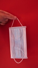 Mano con un guante de látex sujetando una mascarilla con un fondo rojo