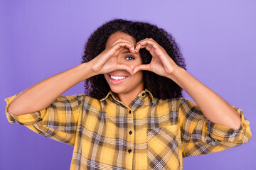 Photo of charming positive afro american woman show fingers heart shape eye look isolated on purple color background