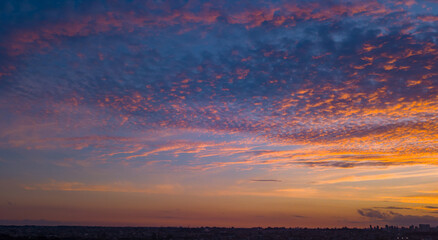 End of the day with a sky between clouds and very colorful, highlighting blue and orange. At the base of the image, and in the background, is the silhouette of the city.
