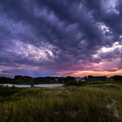 Swirling dramatic purple and blue clouds over marshland lake at sunrise on Cape Cod