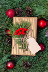 Fototapeta na wymiar A gift box in a craft wrapper with a branch of a fir tree, mistletoe, a wooden blank form for greeting text in branches of a Christmas tree with red toy balls and cones. Christmas and New Year decor