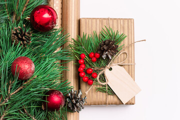 A gift box with mistletoe, a wooden blank form for greeting text, craft wrapper, a branch of a Christmas tree with red toy balls and cones on a white background. New Year's decorations