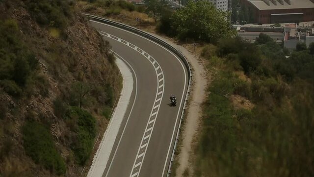 Fast riding of a motorcyclist on an empty road. Roadside of the city top view. A sharp turn along the hill overlooking city.