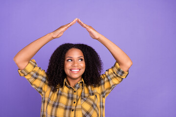 Obraz na płótnie Canvas Photo of dreamy happy afro american woman look empty space hands roof above head isolated on purple color background
