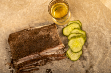 A piece of homemade bacon with pepper, a glass of homemade moonshine and chopped pickles close-up, selective focus.