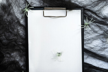 Halloween concept. A notebook with a blank sheet of paper on a background of black cobwebs and spiders.