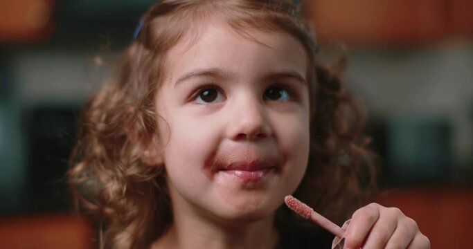 Cute toddler girl applying makeup by herself.