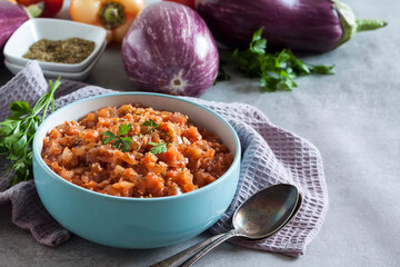 Eggplant caviar in blue bowl and fresh vegetables on background