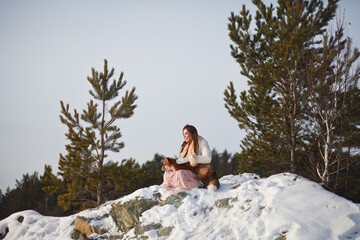 A beautiful girl walks with a fox in a snowy forest. Cold weather. Winter's Tale. Red fox. Photoshoot in a fairy-tale style.