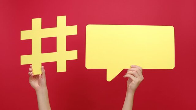Female hands holding yellow paper hashtag symbol and speech bubble, hash sign of famous media content, isolated on red background studio. Post viral web network, blogging blog website strategy concept