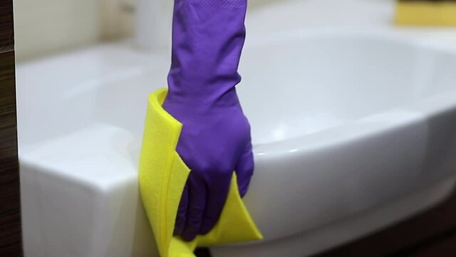 Male hands in rubber gloves wiping a sink and water tap. Man with rag doing chores in bathroom. Housework cleaning concept.