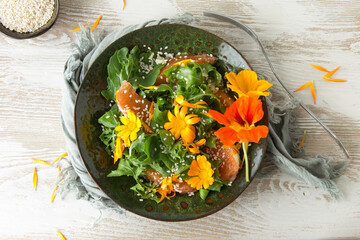 flat lay of green plate with arugula, orange, sesame seeds and edible marigold flowers salad on...