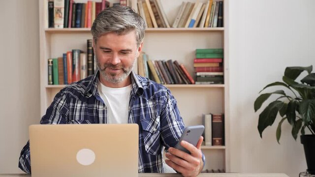 Smart male professional holding modern smartphone texting message at homeoffice. Smart businessman using helpful mobile apps for business time management organization concept sitting at work desk.