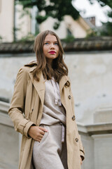 Fototapeta premium Portrait of fashionable women in beige sports suit and trench coat posing on the street