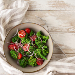 flat lay of a bowl with broccoli and cherry tomato salad on a light table, space for text