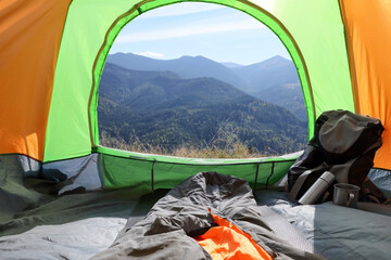 Camping tent with sleeping bag and backpack in mountains, view from inside