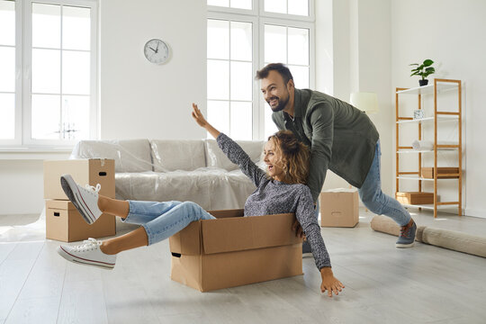 Happy young married couple having fun on moving day. Excited boyfriend and girlfriend playing with boxes in modern interior of new home. Real estate, first time buyers, buying dream house concept