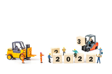 miniature worker team building standing front of forklift machine with white 2022 number on wooden block on white background.