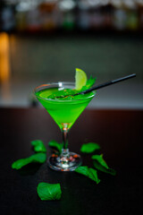 Glass of green cocktail on bar counter with mint and lemon. Selective focus