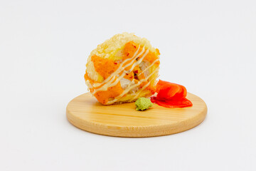 Still life with hot fried sushi roll on a round wooden plate with pickled pink ginger and green wasabi isolated on white background. Tempura roll garnished with hot sauce and mayonnaise.