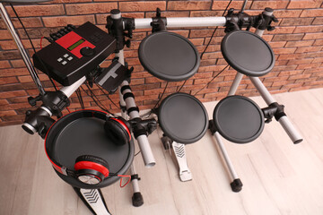 Modern electronic drum kit with headphones near red brick wall indoors, above view. Musical instrument