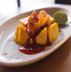 Plate of chopped mango with Mexican chamoy sauce and blurry background