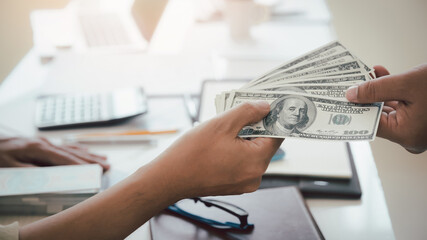 Fototapeta premium Man offering batch of hundred dollar bills. Hand of a businessman giving money to his partner. Hand receiving money from businessman. Venality, bribe, corruption concept.