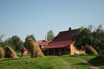 Summer rural landscape with haystacks and wooden country house.