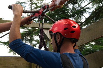 Man prepare to have a fun on zipline among the tops of firs.	