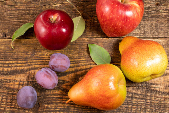 Fresh fruit lying on a wooden table.Apples, pears, fresh leaves and plums on a wooden background.