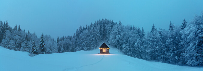 Fantastic winter landscape with glowing wooden cabin in snowy forest. Cozy house in Carpathian...