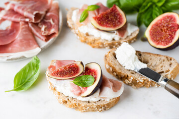 Toast or bruschetta with ricotta cheese, prosciutto and figs on white marble, closeup view